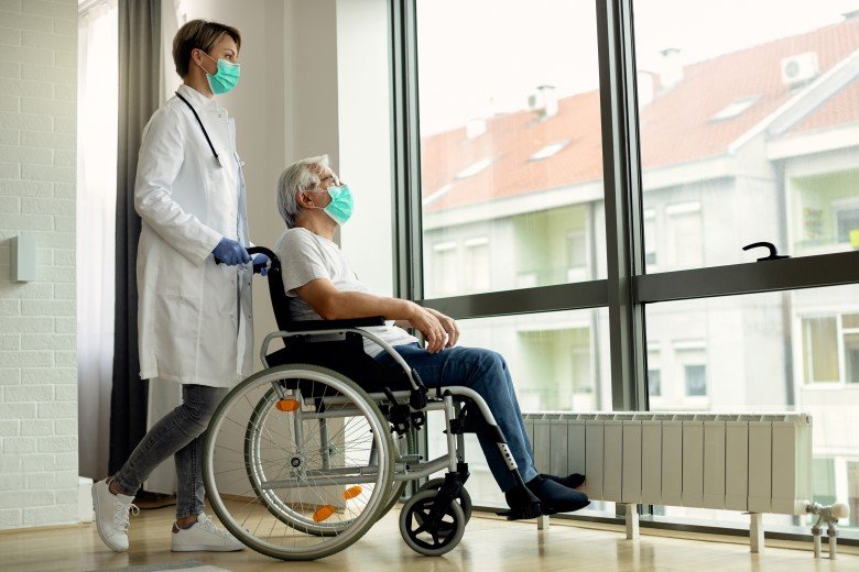 Healthcare professional assisting a senior patient in a wheelchair inside a modern nursing home with compassionate care.