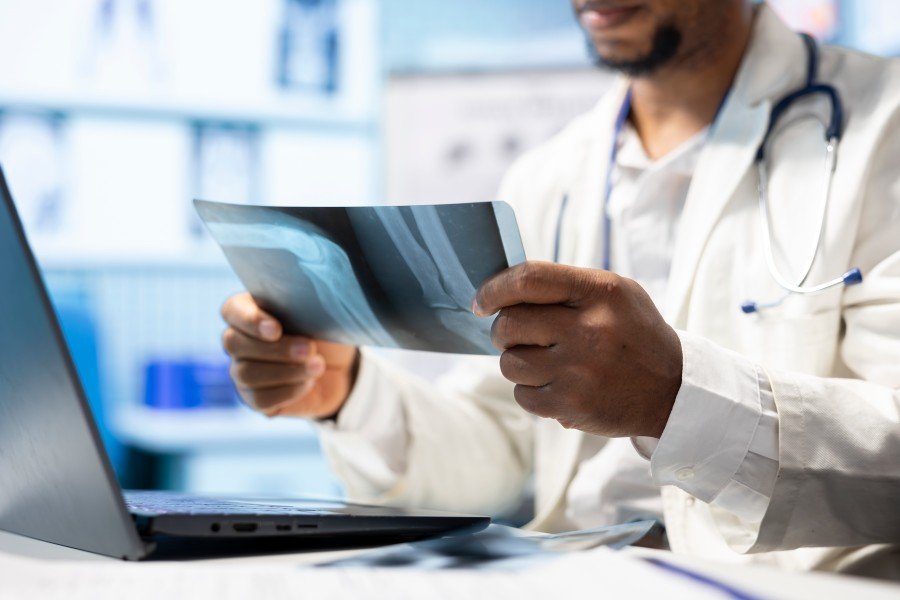 Doctor examining an X-ray image beside a laptop.