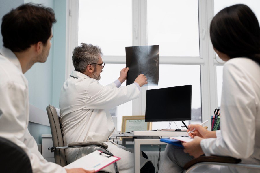 Three doctors in white coats reviewing a radiographic X-ray image in a medical office.