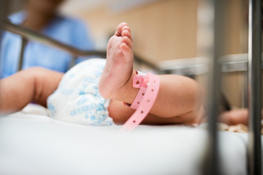 Newborn baby lying in a hospital crib with a medical identification band